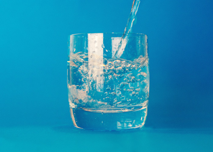 A stream of fluoridated water is being poured into a clear glass of water against a blue background