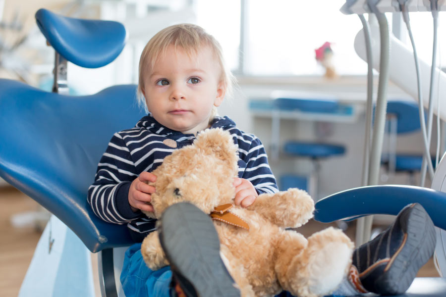 Blond toddler boy in the dental chair with his teddy bear.