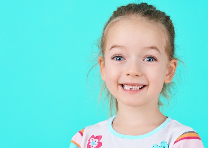 Blonde little girl smiles against an aqua background after losing her first loose baby tooth